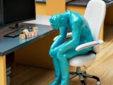 a statue of a person sitting in a chair in front of a computer