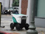 A small delivery robot with googly eyes on a sidewalk.