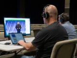 man in black shirt wearing black headphones sitting on beige chair