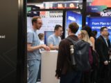 People interacting at a busy trade show booth.