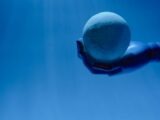 A robotic hand holds a glowing celestial sphere against a blue background, evoking a futuristic theme.