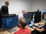 a group of men sitting at a table working on computers