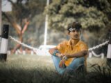 woman in orange polo shirt and blue denim jeans sitting on brown grass field during daytime