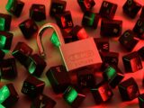 An open padlock surrounded by scattered black computer keyboard keys under red and green light