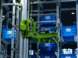 High-tech automated warehouse system featuring a green robotic arm handling blue storage crates.