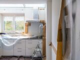 A kitchen under renovation with white cabinets covered in plastic and brown paper